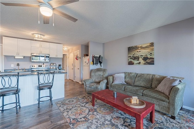 living room featuring ceiling fan, dark hardwood / wood-style floors, sink, and a textured ceiling