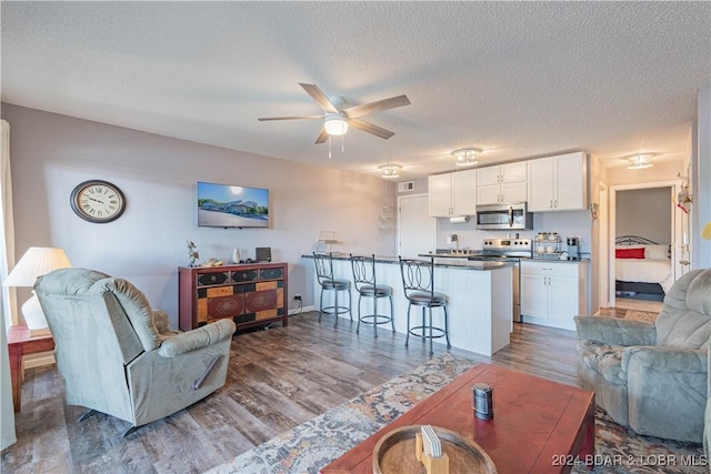 living room with ceiling fan, wood-type flooring, and a textured ceiling