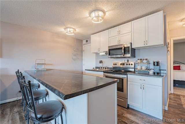 kitchen featuring appliances with stainless steel finishes, white cabinetry, dark hardwood / wood-style flooring, a kitchen breakfast bar, and a textured ceiling