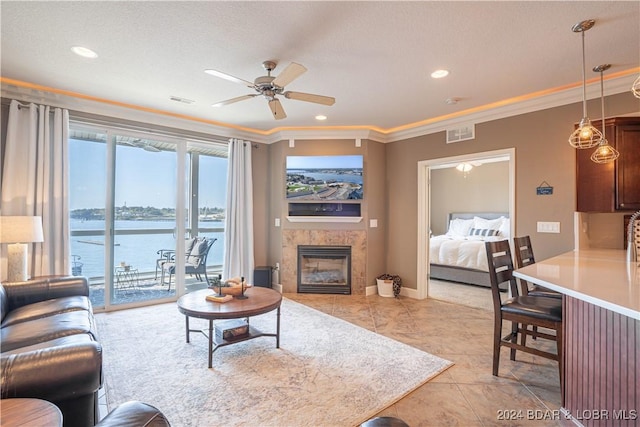 living room with a water view, a fireplace, a ceiling fan, visible vents, and crown molding