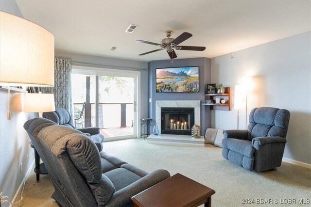 carpeted living room with a high end fireplace and ceiling fan