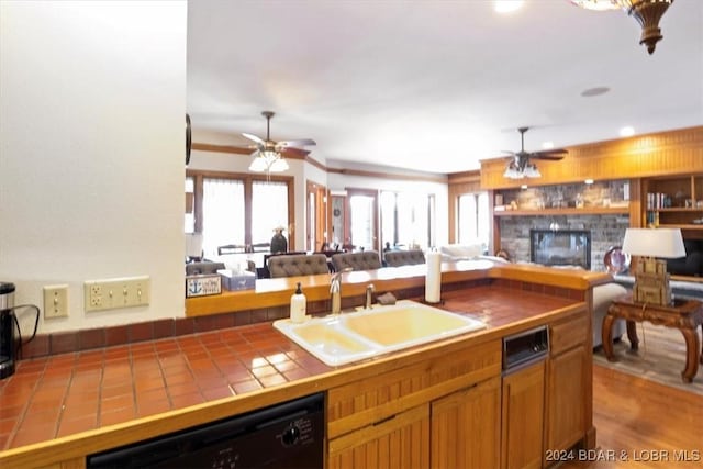 kitchen featuring sink, dishwasher, hardwood / wood-style floors, a stone fireplace, and tile counters