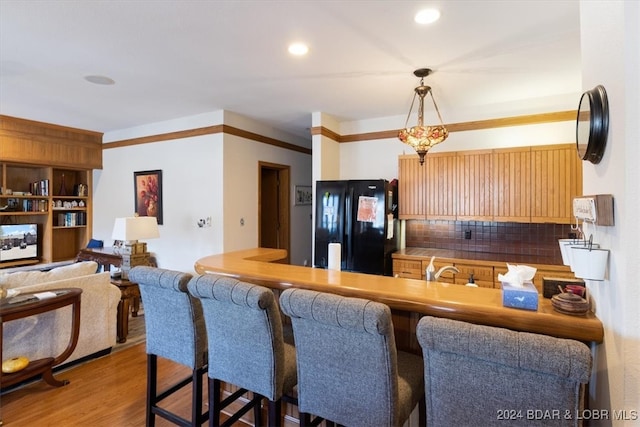 kitchen featuring tasteful backsplash, black fridge, ornamental molding, pendant lighting, and light hardwood / wood-style floors