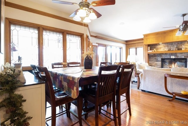 dining room featuring a fireplace, light hardwood / wood-style floors, ceiling fan, and ornamental molding