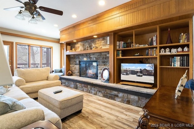 living room with built in features, wood-type flooring, a stone fireplace, and ceiling fan