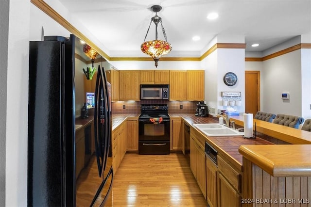 kitchen featuring decorative backsplash, sink, black appliances, decorative light fixtures, and light hardwood / wood-style flooring