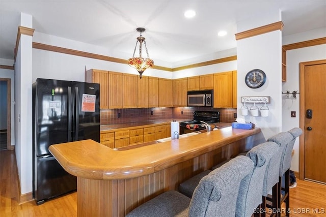 kitchen featuring kitchen peninsula, light wood-type flooring, tasteful backsplash, black appliances, and hanging light fixtures