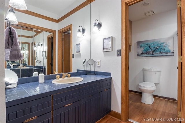 bathroom featuring toilet, vanity, wood-type flooring, and ornamental molding