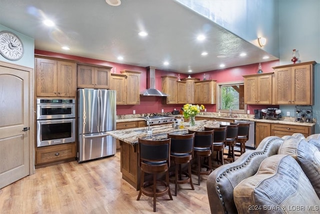 kitchen with a breakfast bar, light wood-type flooring, a kitchen island, wall chimney exhaust hood, and appliances with stainless steel finishes