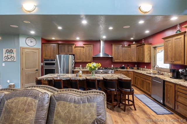 kitchen with a breakfast bar, wall chimney exhaust hood, a kitchen island, stainless steel appliances, and sink