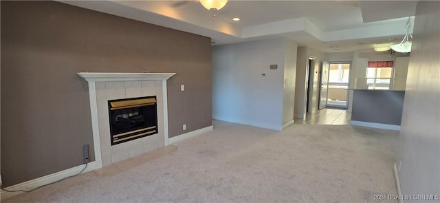 unfurnished living room featuring a raised ceiling, light colored carpet, and a tiled fireplace