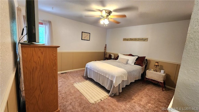 carpeted bedroom featuring ceiling fan and wooden walls