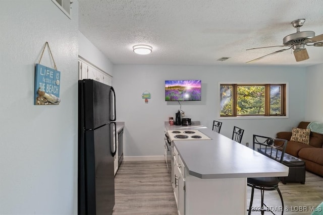 kitchen with a textured ceiling, a kitchen bar, white cabinets, black appliances, and light wood-type flooring