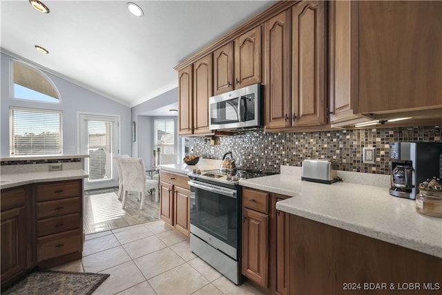 kitchen with appliances with stainless steel finishes, light tile patterned floors, lofted ceiling, and light stone counters