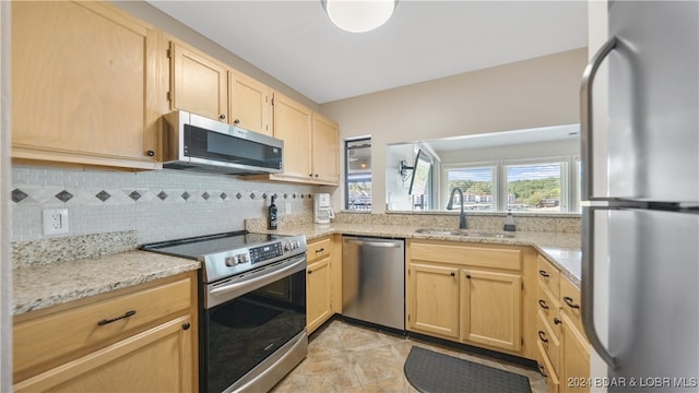 kitchen featuring light brown cabinetry, sink, stainless steel appliances, light stone countertops, and backsplash