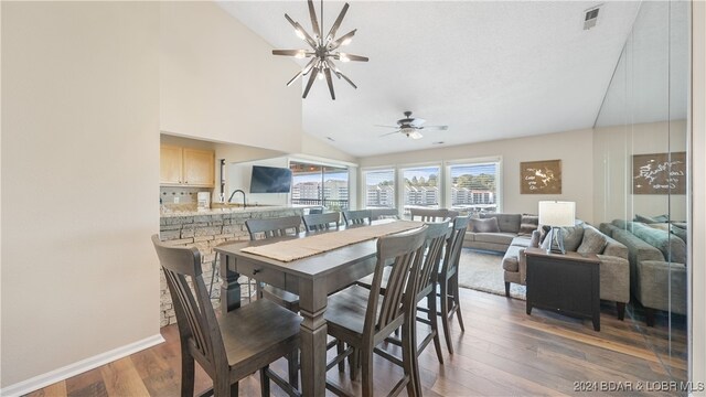 dining area with lofted ceiling, ceiling fan with notable chandelier, and dark hardwood / wood-style flooring