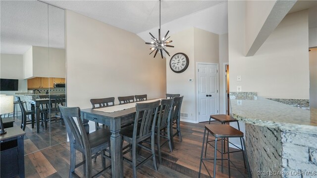 dining space featuring an inviting chandelier, a textured ceiling, dark hardwood / wood-style floors, and vaulted ceiling