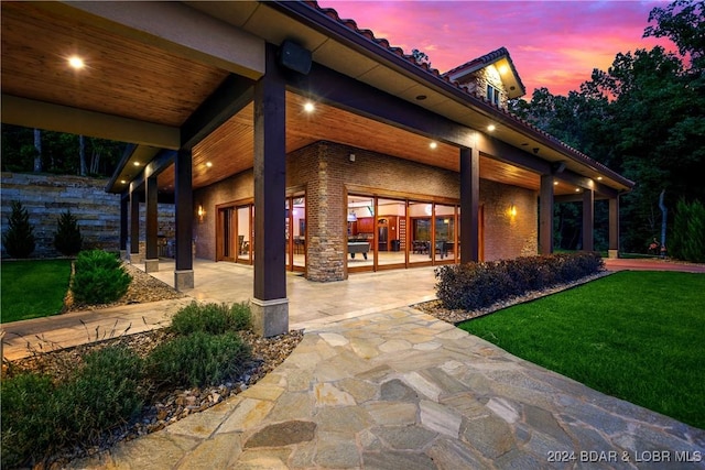 patio terrace at dusk featuring a lawn