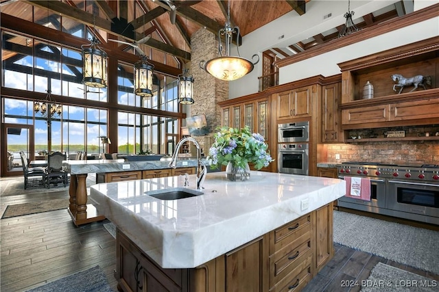 kitchen with beam ceiling, dark wood-type flooring, high vaulted ceiling, a center island with sink, and appliances with stainless steel finishes