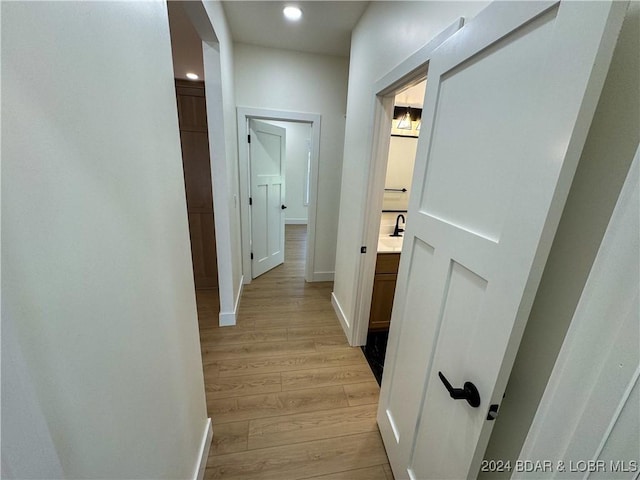 hall featuring recessed lighting, light wood-type flooring, a sink, and baseboards