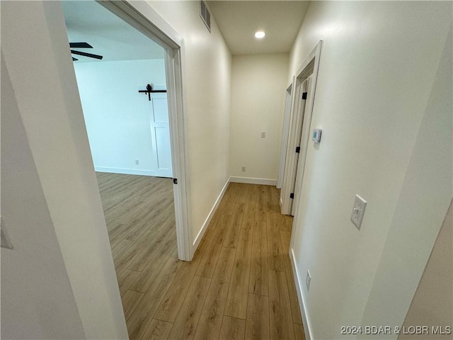 hall with a barn door, light wood-type flooring, visible vents, and baseboards