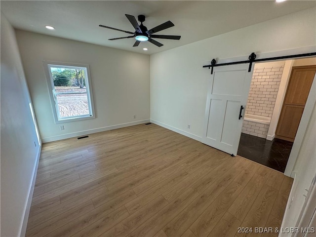 unfurnished bedroom featuring baseboards, a barn door, recessed lighting, and light wood-style floors