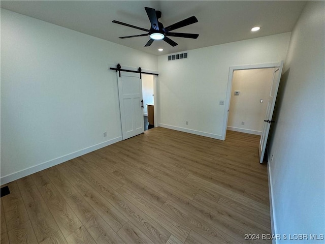 unfurnished bedroom with baseboards, a barn door, visible vents, and light wood-style floors