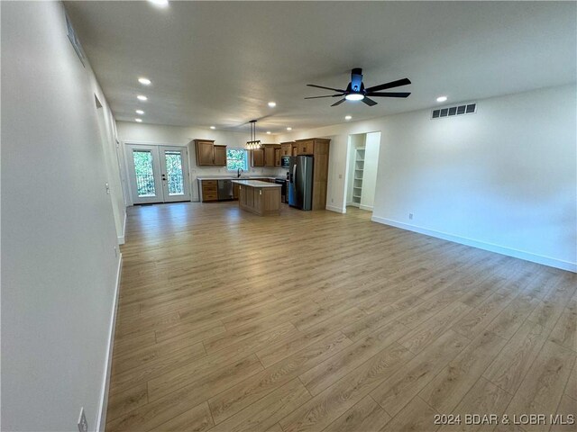 unfurnished living room with ceiling fan, sink, light hardwood / wood-style flooring, and french doors