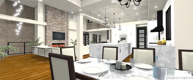 dining room with a stone fireplace, wood-type flooring, a high ceiling, and a chandelier