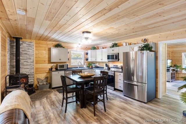 dining room with light hardwood / wood-style floors, a wood stove, wooden walls, and wooden ceiling