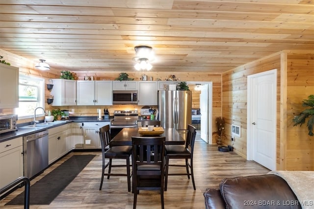 kitchen featuring sink, wooden walls, appliances with stainless steel finishes, and white cabinets