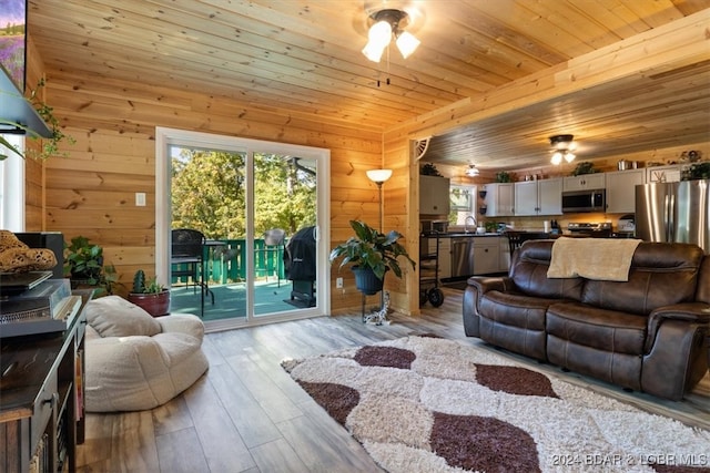 living room with light hardwood / wood-style flooring, wood walls, wooden ceiling, and ceiling fan