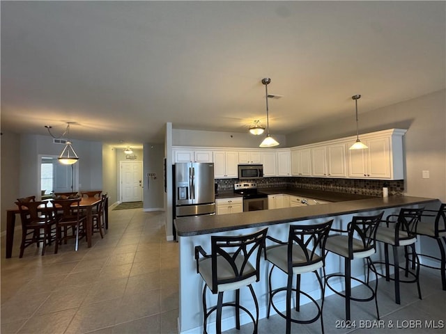 kitchen featuring kitchen peninsula, decorative backsplash, decorative light fixtures, white cabinetry, and stainless steel appliances