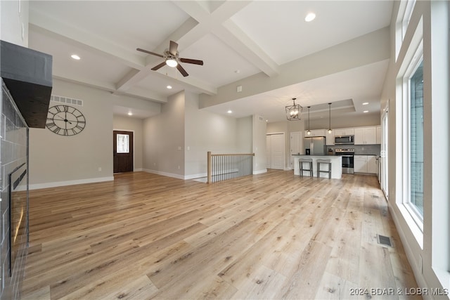 unfurnished living room featuring beamed ceiling, light hardwood / wood-style flooring, and a wealth of natural light