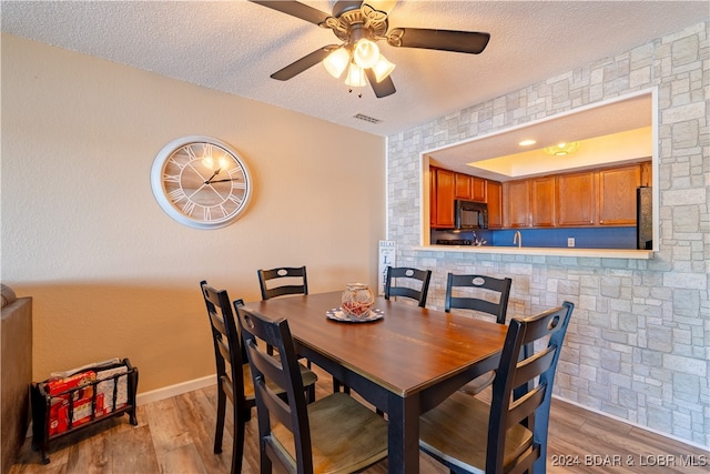 dining space with ceiling fan, a textured ceiling, tile walls, and light hardwood / wood-style floors