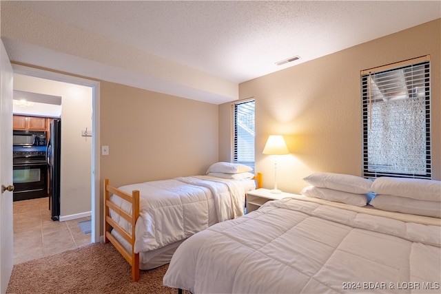 bedroom featuring light tile patterned floors, a textured ceiling, and black refrigerator