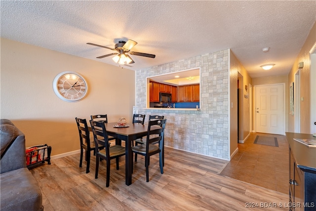 dining space with ceiling fan, a textured ceiling, tile walls, and light hardwood / wood-style flooring