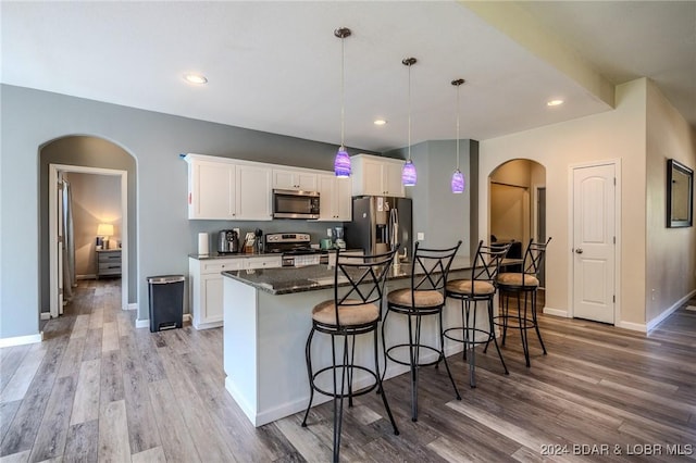 kitchen featuring stainless steel appliances, decorative light fixtures, dark stone countertops, a center island, and white cabinetry