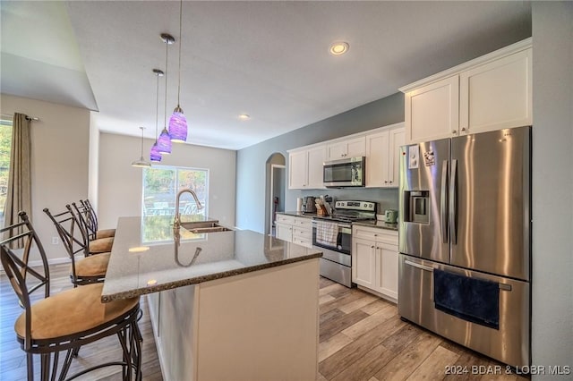 kitchen with sink, an island with sink, a kitchen bar, white cabinetry, and stainless steel appliances