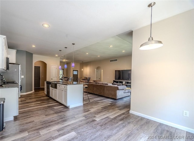 kitchen with white cabinets, decorative light fixtures, a center island with sink, and light wood-type flooring