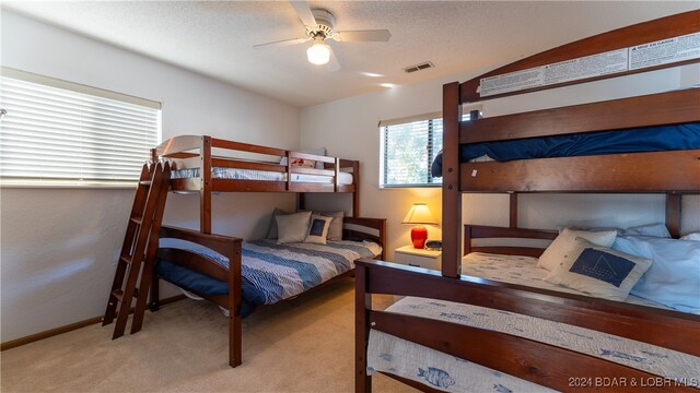 bedroom featuring a textured ceiling, light colored carpet, and ceiling fan