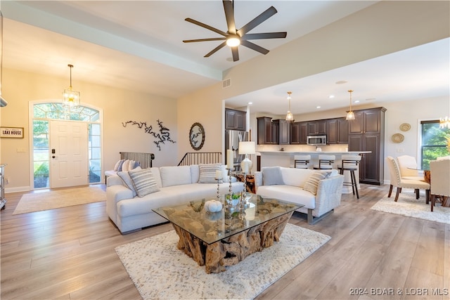 living room with ceiling fan with notable chandelier and light hardwood / wood-style flooring