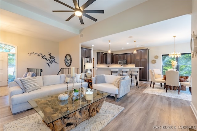 living room featuring ceiling fan with notable chandelier, a healthy amount of sunlight, and light hardwood / wood-style floors