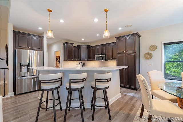 kitchen with pendant lighting, appliances with stainless steel finishes, tasteful backsplash, and light hardwood / wood-style flooring