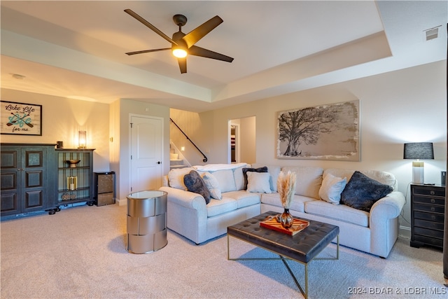 living room with ceiling fan, a raised ceiling, and light colored carpet