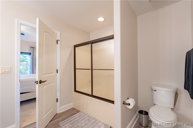 bathroom featuring toilet, combined bath / shower with glass door, and hardwood / wood-style flooring