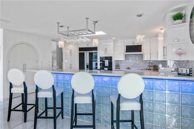 kitchen with black built in refrigerator, backsplash, custom exhaust hood, hanging light fixtures, and white cabinets