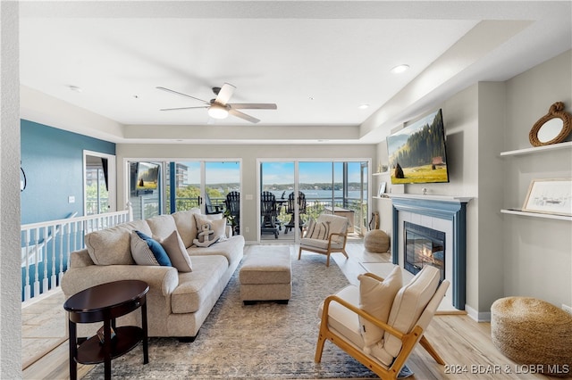 living room featuring ceiling fan, a tile fireplace, light hardwood / wood-style floors, and a healthy amount of sunlight