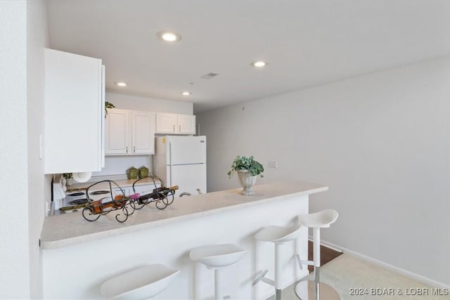 kitchen with recessed lighting, a breakfast bar, white cabinetry, light countertops, and freestanding refrigerator