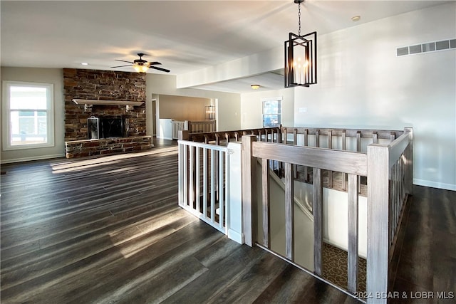 interior space featuring dark hardwood / wood-style floors, a stone fireplace, and ceiling fan with notable chandelier